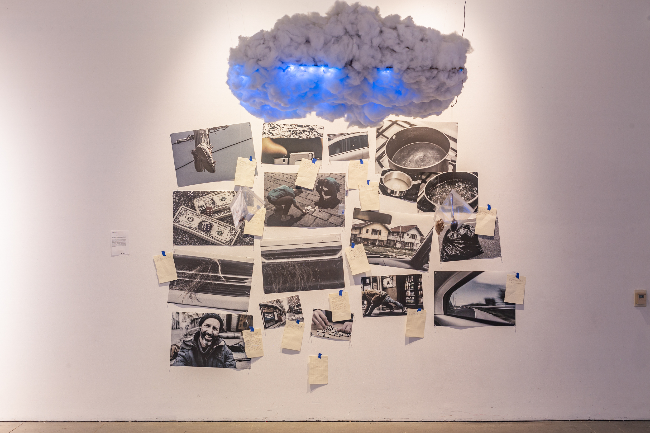 A white wall with a fabricated cloud above, on the wall are several AI-generated photo prints.